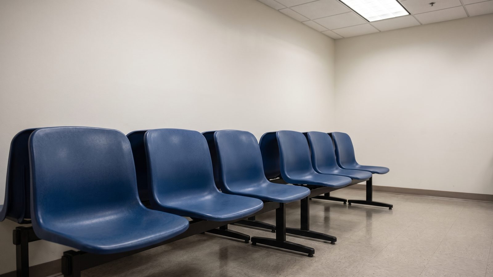 A row of empty blue molded-plastic waiting chairs in a government field office under fluorescent light